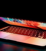 a laptop against a black background is partly open and glowing rainbow colors like magic
