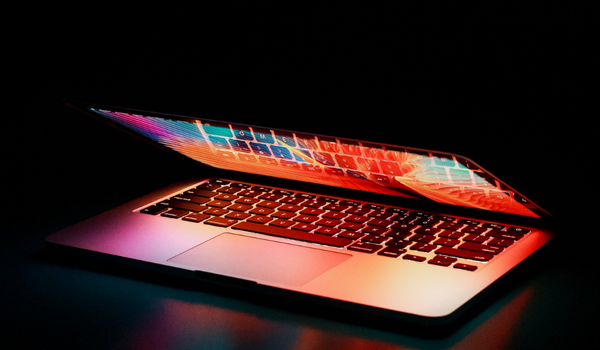 a laptop against a black background is partly open and glowing rainbow colors like magic