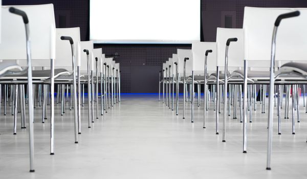 White chairs lined up in an empty room with a white projector screen at the front.